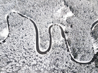 Fototapeta na wymiar Winding road among a snowy forest, from high mountain pass, winter weather. Aerial view by drone. Romania