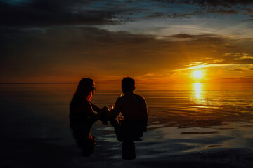 Young couple in love enjoying a red sunset on a beach sitting in the water.