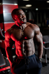 Fototapeta na wymiar Sport portrait of african american athlete. Strong bodybuilder man posing in gym. Dark colours portrait.