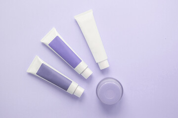 three tubes with cosmetic creams, one jar with cosmetics on a lilac background, beauty concept 