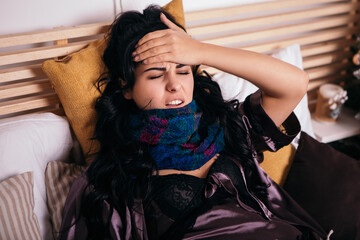 Upset woman lying in bed scarf heat hyperthermia headache at home. Lady got sick ill fever cold...