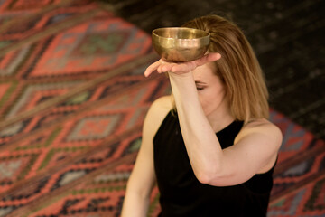 Woman playing on Tibetan singing bowl while sitting on yoga mat. Vintage tonned.