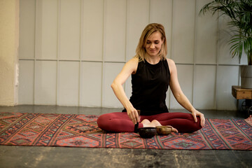 Woman playing on Tibetan singing bowl while sitting on yoga mat. Vintage tonned.