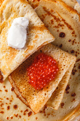 Traditional Russian Crepes Blini stacked in a plate with red caviar, fresh sour cream on light background. Maslenitsa traditional Russian festival meal. Russian food, russian kitchen. Close up.
