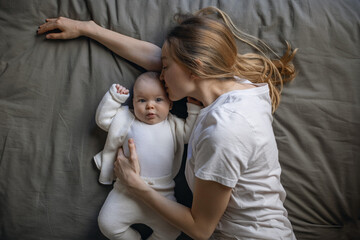 Mom with her baby lies and looks at the camera from the top. Beautiful young woman with her baby. Mother and daughter. Happy family.