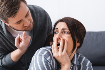  husband pointing with finger near scared woman with bruise on cheek covering mouth