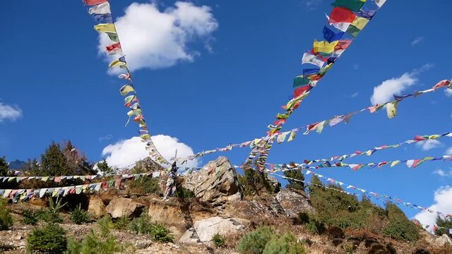 Several lines multi-colored Buddhist prayer flags peacefully flying in the wind above Namche Bazar, Khumbu, Himalayas, Nepal on sunny day with blue sky and few clouds.