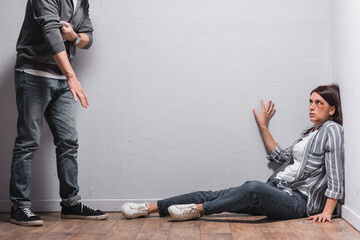  woman with bruises sitting on floor near abuser rolling up sleeves