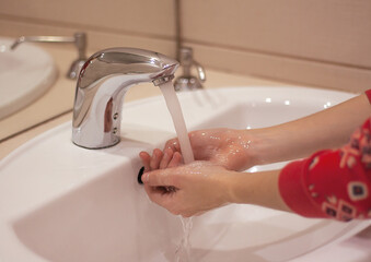 hands of a girl close-up under running water over a white sink. hand washing and hygiene concept.