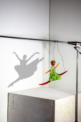 Ballerina made of cabbage, spicy pepper, cucumbers. Flying food composition making beautiful sportswoman drawing shadow on the white wall. Concept of sport, nutrition, healthy lifestyle choice.