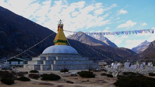 Buddhist stupa (religious monument) in a valley near Thame, Khumbu, Himalayas, Nepal with prayer flags flying in the wind and a wall of mani stones with carved mantras.