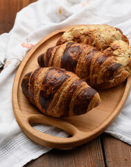 baked croissants lie on a wooden tray, food on a brown background