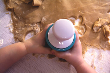 Closeup of a child's hand. The child holds a shape in his hands and cuts cookies from the dough