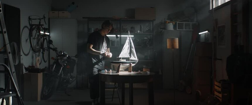 WIDE Caucasian teenager boy placing sails on his boat model school project inside his home garage. Shot with 2x anamorphic lens