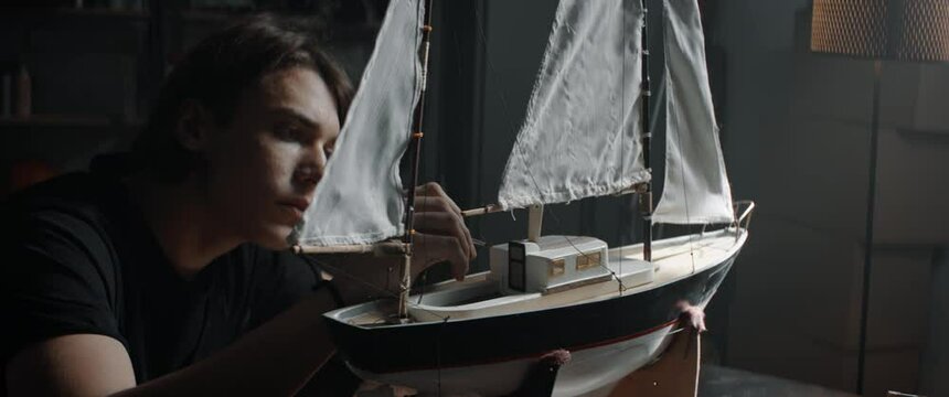 CU Portrait of Caucasian teenager boy making finishing paint touches on his custom built vessel school model project. Shot with 2x anamorphic lens
