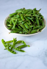 Peas. Green pea pods in a plate on a white table. Harvest. Healthy food close-up. Copy space.