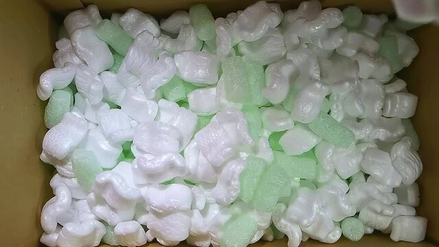 green foam rubber and white styrofoam chips filler falls into a cardboard box for packing, slow motion