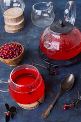 Hot cranberry tea in a glass Cup and a teapot on a dark cold background. Warming and healing tea with berries. New year's drink for a cozy evening.