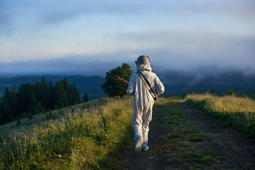 Back view of space traveler walking on mountain road and playing melody on guitar. Cosmonaut...