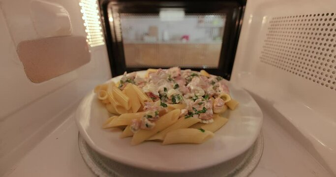 Heating food in a microwave viewed from inside the back, grabbing plate of pasta with salmon when it's done signaled by a chime ding sound