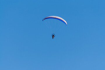 Silhouette of a man flying on a hang glider. In the background is a blue sky without clouds.