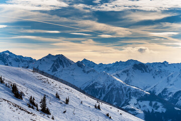 Snowy mountain peaks in the Zell am See area of Austria. In the background is a blue sky with dramatic clouds.