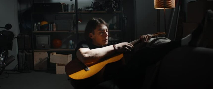 HANDHELD WIDE to CU Caucasian teenager boy entering his home garage hideout, grabbing acoustic guitar. Shot with 2x anamorphic lens