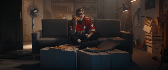 POV Portrait of Caucasian teenager playing video game inside home garage, enjoying pizza. Shot with 2x anamorphic lens