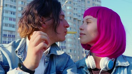 A woman and man in love eating french fries together. A young loving couple against an apartment building
