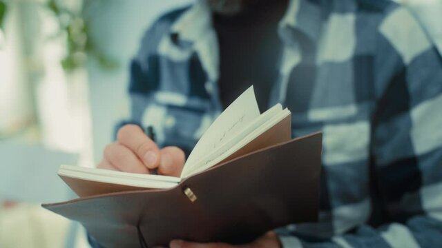 Man write down text notes with pen in leather paper notebook. Learning new skills, or writing down diary during lecture or class. Old fashioned planning skills. Write with pen in vintage notebook
