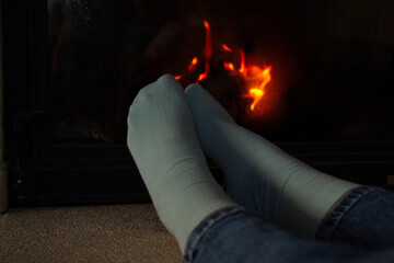 A girl's legs in blue socks are warm by the burning fireplace