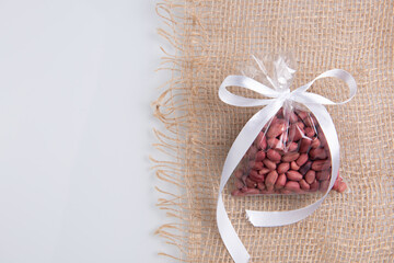 peanuts in a gift transparent package tied with a white ribbon on a burlap on a white background