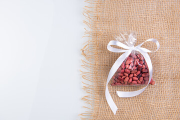 peanuts in a gift transparent package tied with a white ribbon on a burlap on a white background