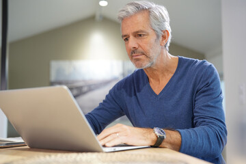 Portrait of senior man at home working on laptop