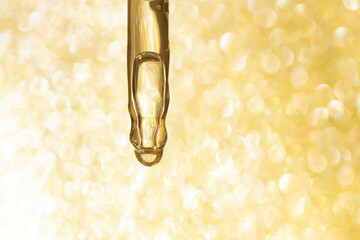 detail of pipette dropper with beauty serum on a golden glitter shimmering background