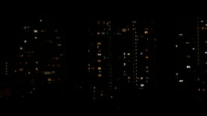 Night city view with lights in windows of multistory buildings in darkness. Defocus lights of residential house windows. Urban abstraction in big city