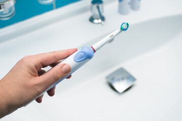 Electric oscillating toothbrush in woman hand in bathroom at home