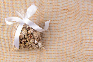 peanuts in kujut in a gift transparent package tied with a white ribbon on a burlap on a white background