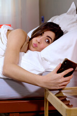 Funny woman in bed in the morning making faces taking selfie with cell phone