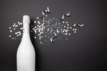 Champagne bottle and confetti on dark background. Flat lay of celebration composition. Top view....