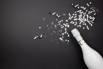 Champagne bottle and confetti on dark background. Flat lay of celebration composition. Top view. Copy space.