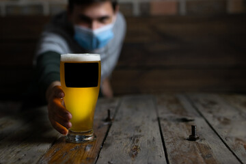 Take the glass of beer by the hand on the wooden table. He stretches for the glass of blonde beer.