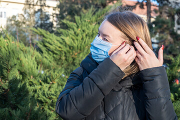 Blonde girl puts on a mask on the street. sunny day, spring.