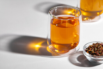 Glass cup of tea and dry tea leaves on white table