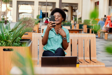 A young African girl with glasses takes a selfie photo on her smartphone, posing in front of the camera. A girl takes a selfie during a break while working on a laptop.
