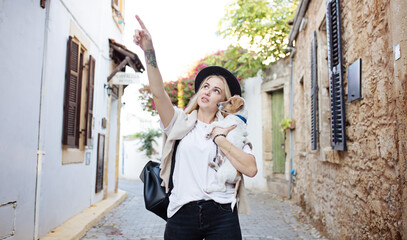 Lifestyle image of happy young woman walking old city street with small jack russell dog.Drinking tea. Wearing stylish minimalistic outfit. Freedom and happiness concept. Tourism and adventure