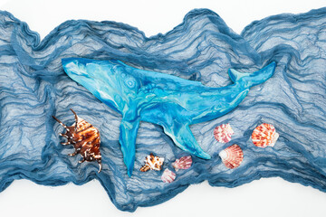 Resin art blue whale with fabric and sea shells on white background. Flat lay