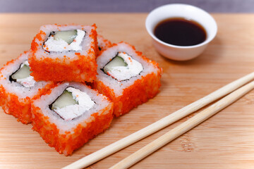 Sushi maki rolls with chopsticks on bamboo table with soy sauce.