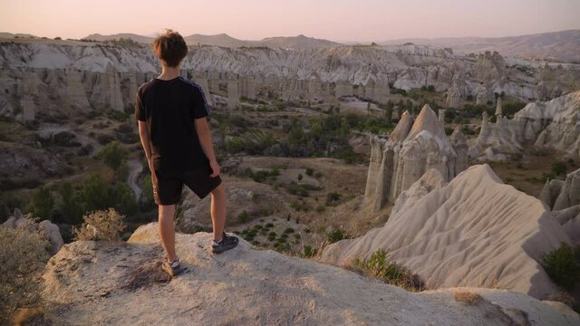Young man stands on mountain top overlooking view and sunset, Love Valley, Cappadocia, Turkey