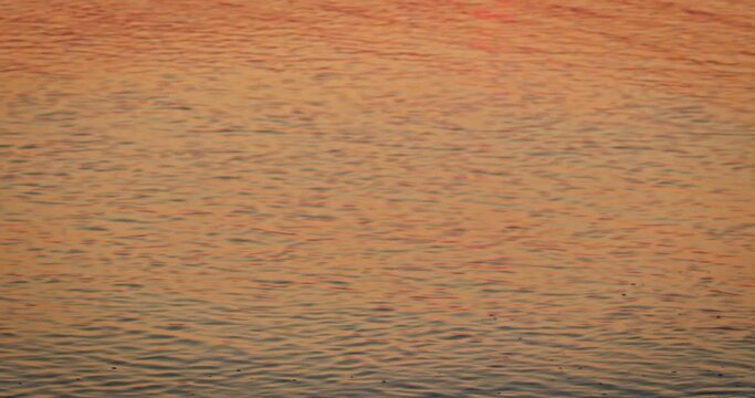 Calm sea with sunset light over the aqua surface. Meditation view at ocean at sundown. Tranquil seascape with ripples on orange seawater surface. Melancholy mood.